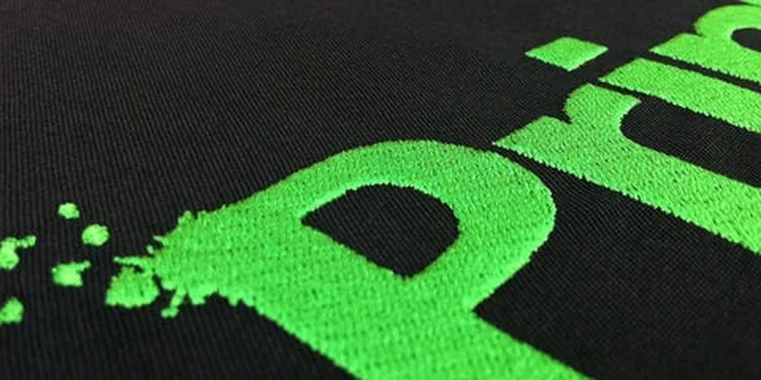 Grün besticktes Logo auf schwarzem Stoff
