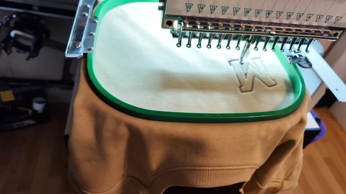 Weißes W-Monogramm wird auf beigen Sweater gestickt