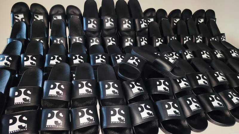 Schwarze Badelatschen mit PS Gerüstbau Logo, viele Paare